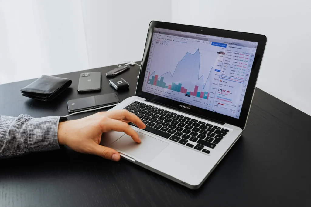 A hand on a laptop tracking stock market data and financial charts, illustrating the need for granular analysis in entity based SEO.