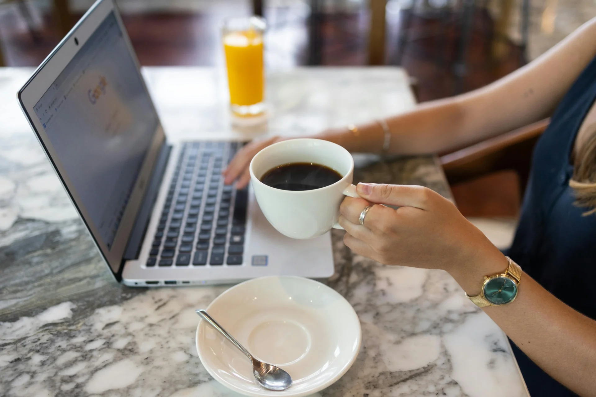 Woman holds a coffee cup while working on a laptop, studying AI trends in marketing at a cafe.