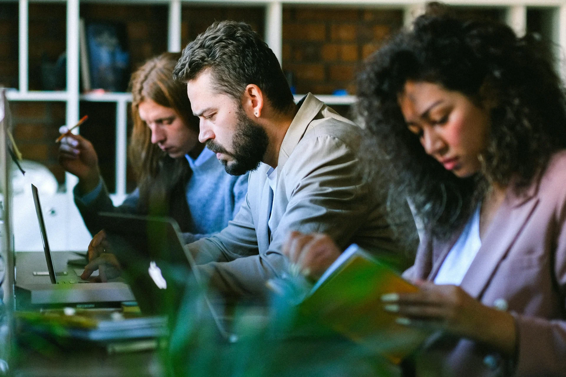 Three colleagues intensely working on laptops and notebooks in an office, discussing how to adapt their content to the generative search impact.
