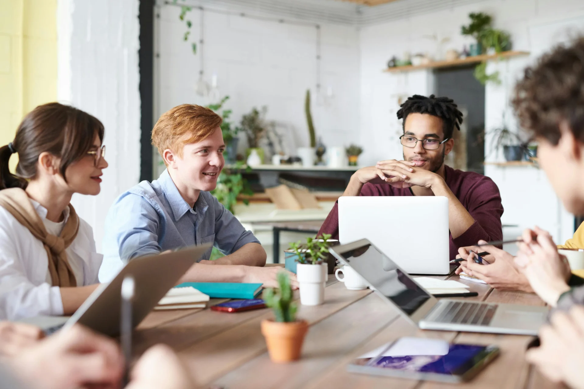 A diverse group of young professionals collaborating around a wooden table in a bright office, discussing brand consistency importance.