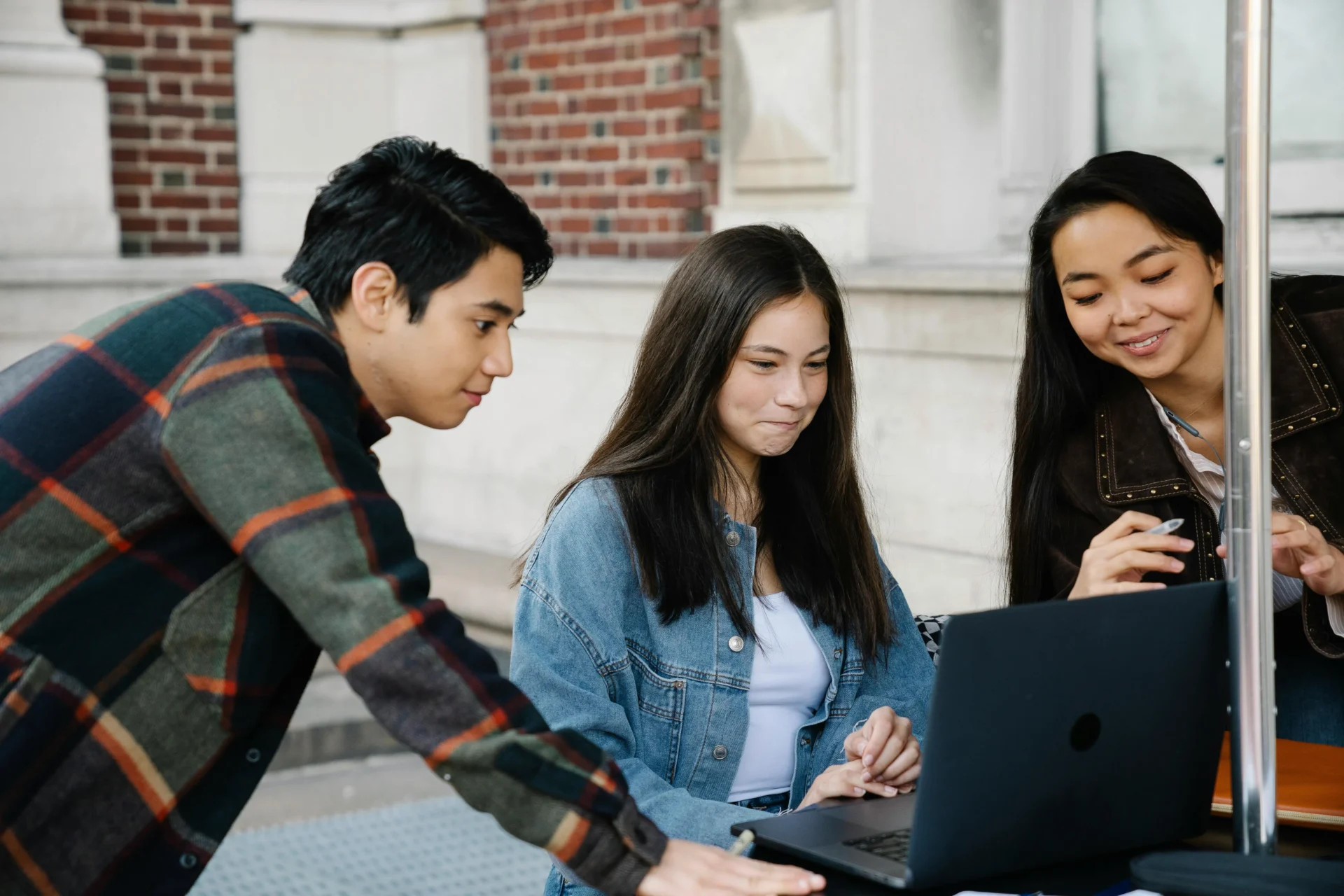 A group of three young professionals looking at a laptop screen together outdoors to strategize and avoid internal keyword competition.
