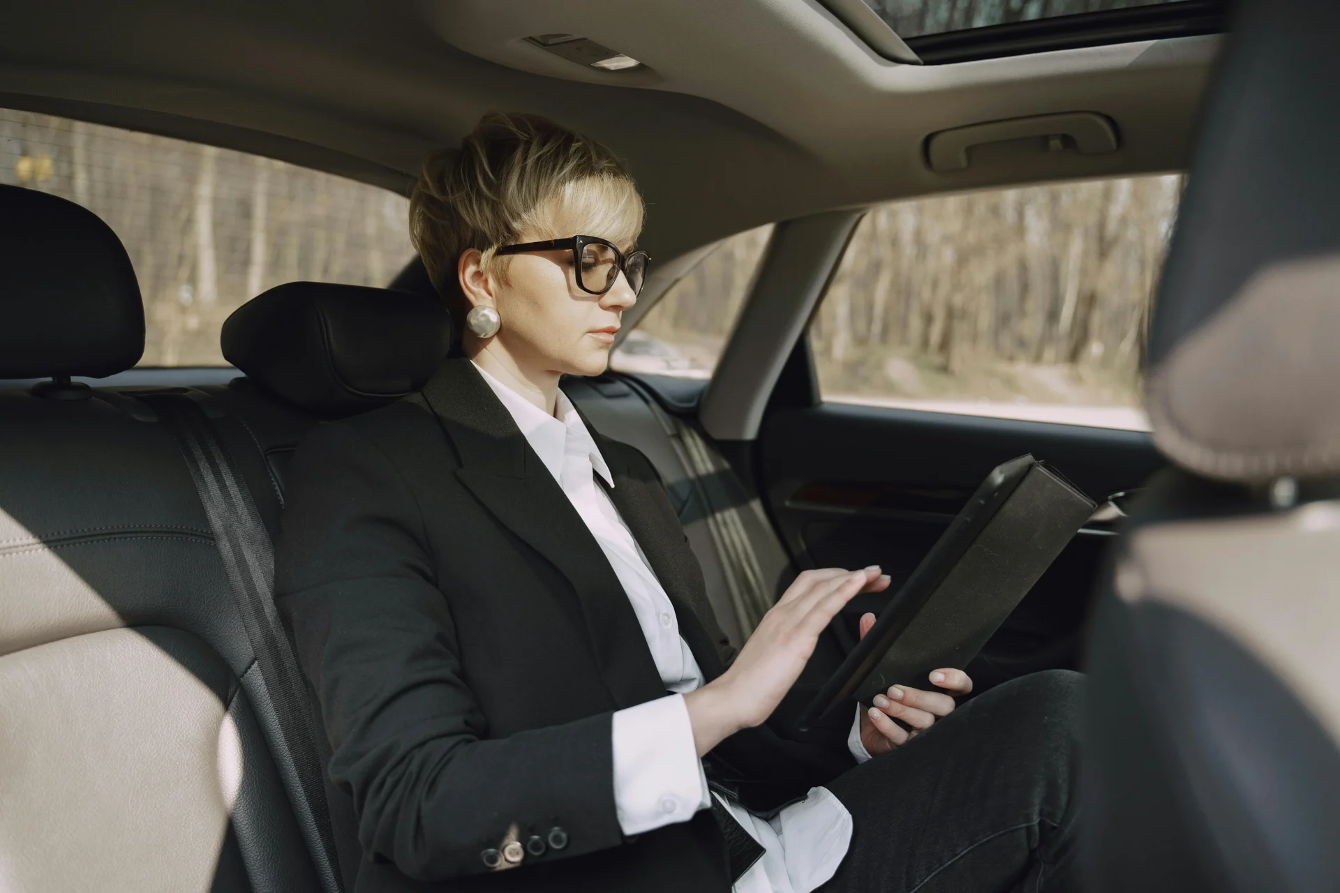 Businesswoman in a suit using a tablet in the backseat of a car to demonstrate how people search while traveling.