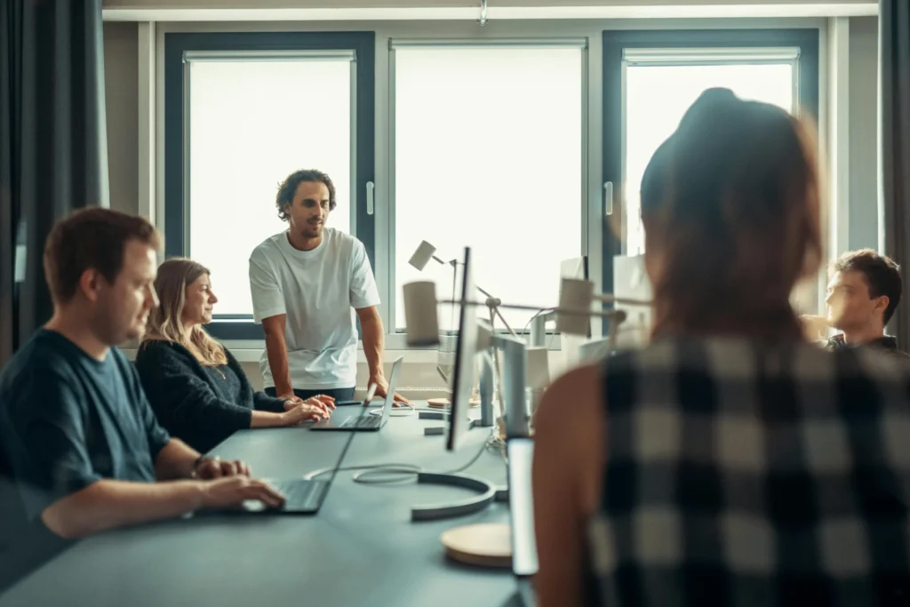 A team of diverse professionals collaborating at a long desk with laptops in a bright, modern office, discussing knowledge graph basics.