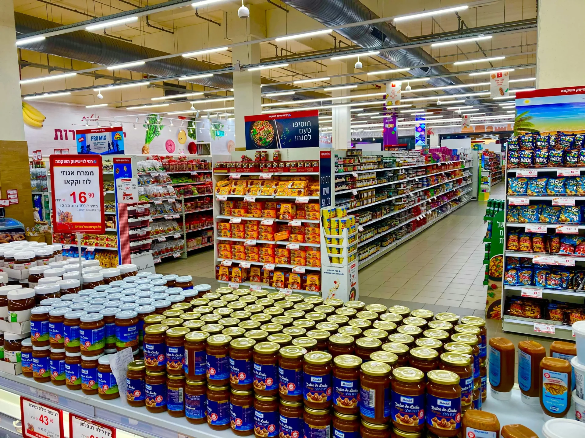 A brightly lit supermarket interior showing organized aisles stocked with various consumer packaged goods.