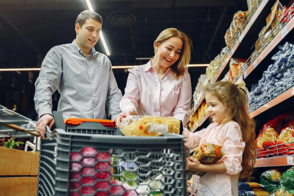 A shopper in a grocery aisle using a smartphone to scan a product barcode for price comparison and reviews.
