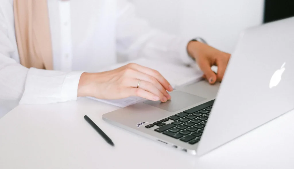 A close-up of a person in a white shirt and beige hijab using a laptop trackpad to study search context signals.