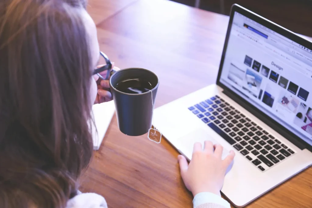 An over-the-shoulder view of a woman analyzing web design layout vs conversion rates on her laptop while holding a cup of tea.