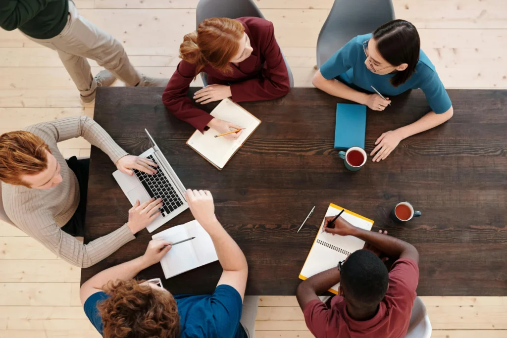 Overhead view of a diverse team brainstorming and writing content for ChatGPT citations around a wooden table.