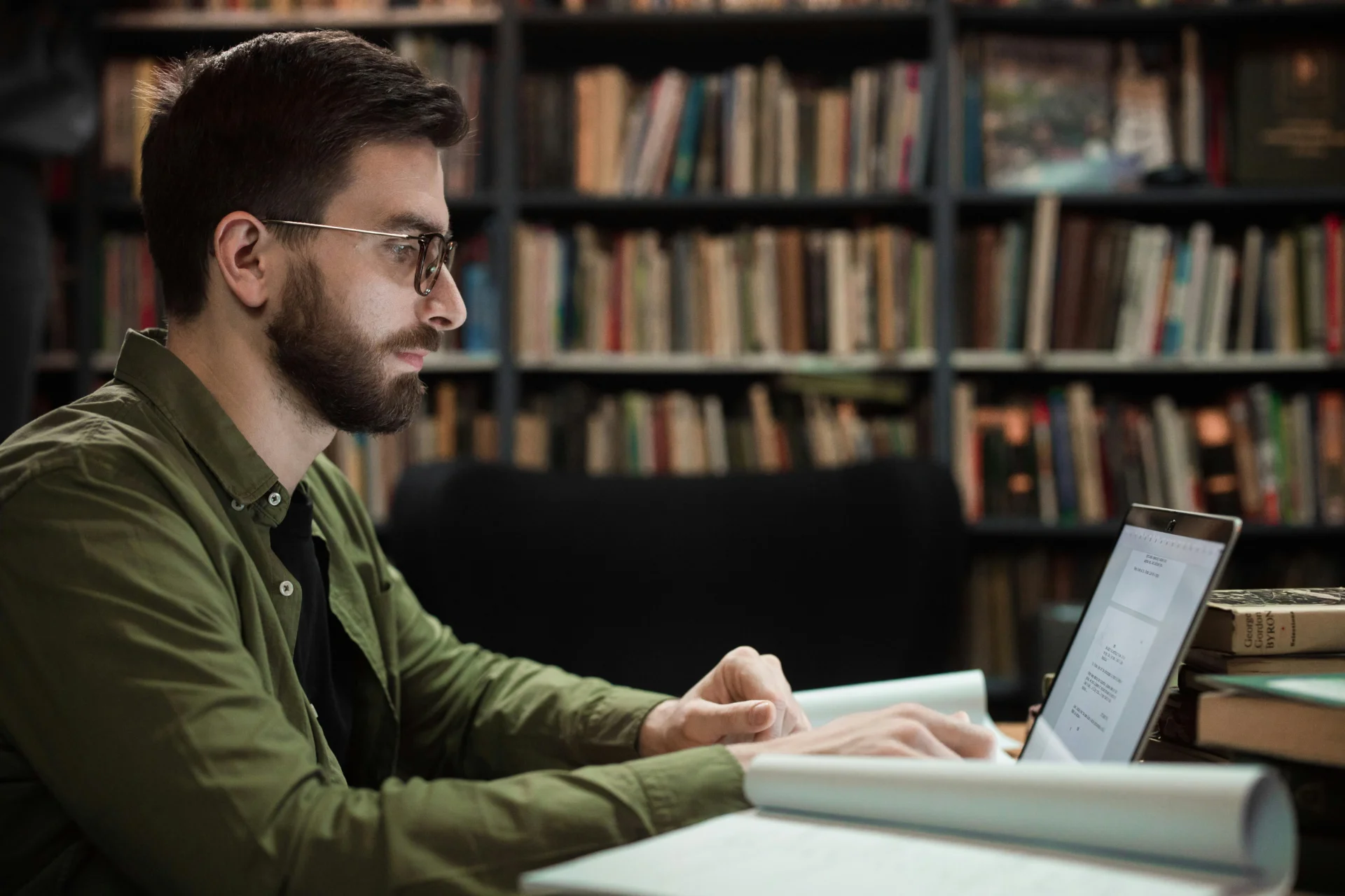 Bearded man with glasses working on a laptop in a library researching which AI engines cite sources,