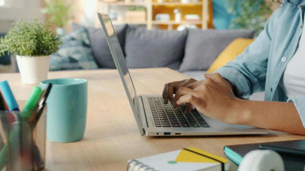 Person typing FAQ content on a laptop at a home desk to use FAQs for AI visibility.