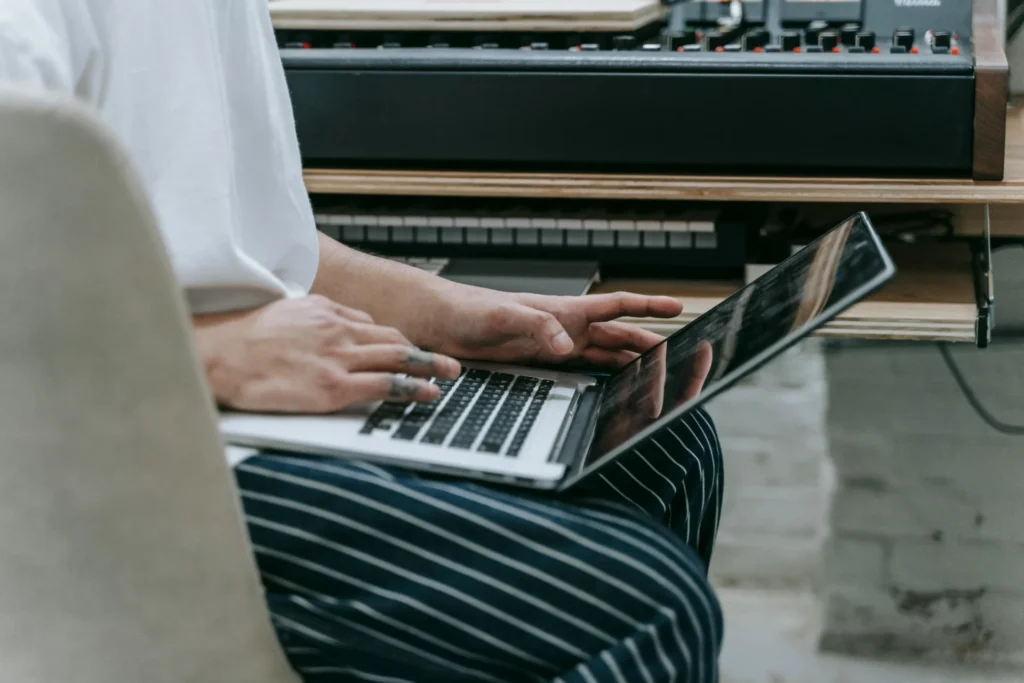 Creative professional using an AI brand visibility tool on a laptop while seated near a music production keyboard setup.