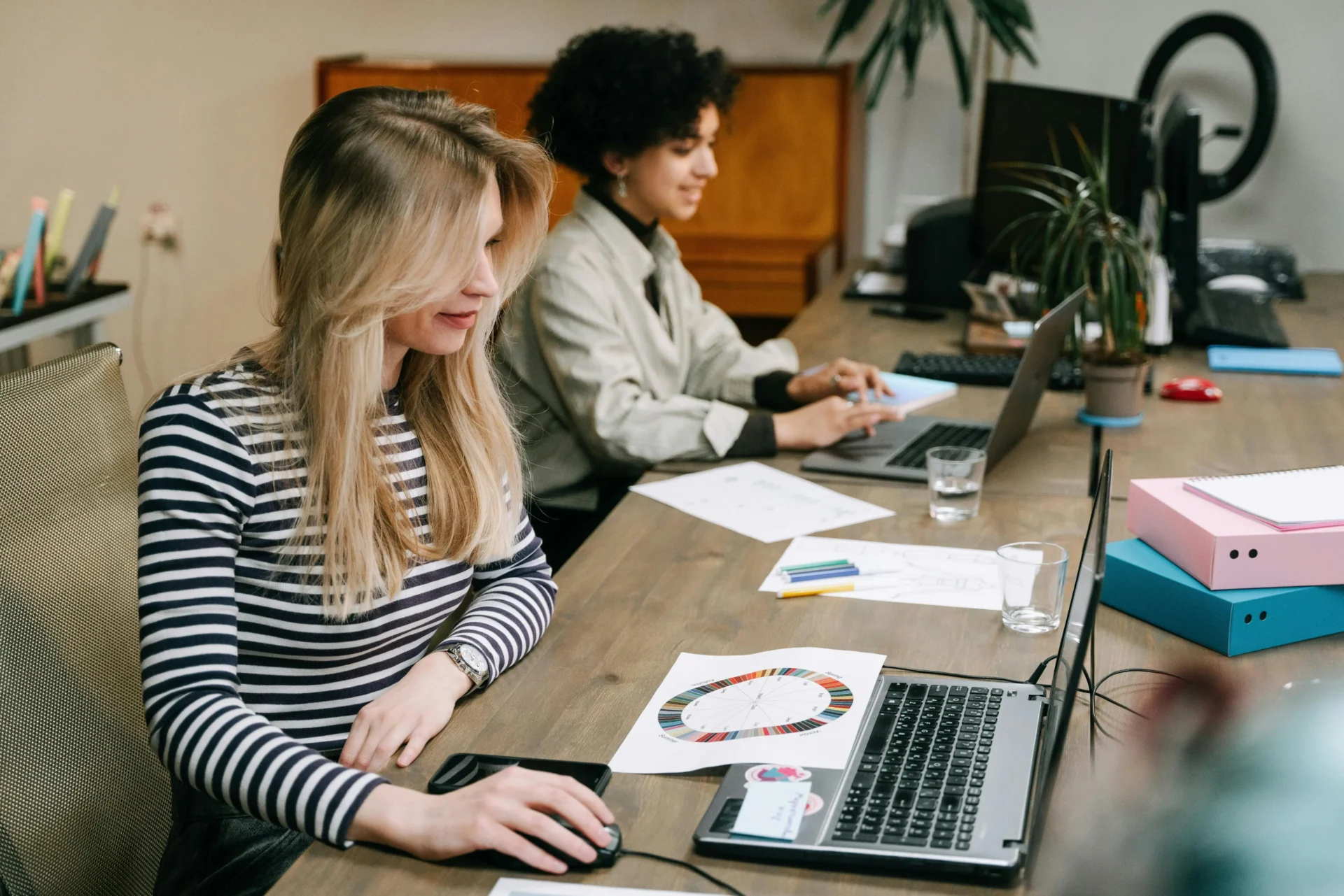 Two marketing professionals working on laptops with color wheel charts and brand materials on desk to measure brand visibility in AI search.