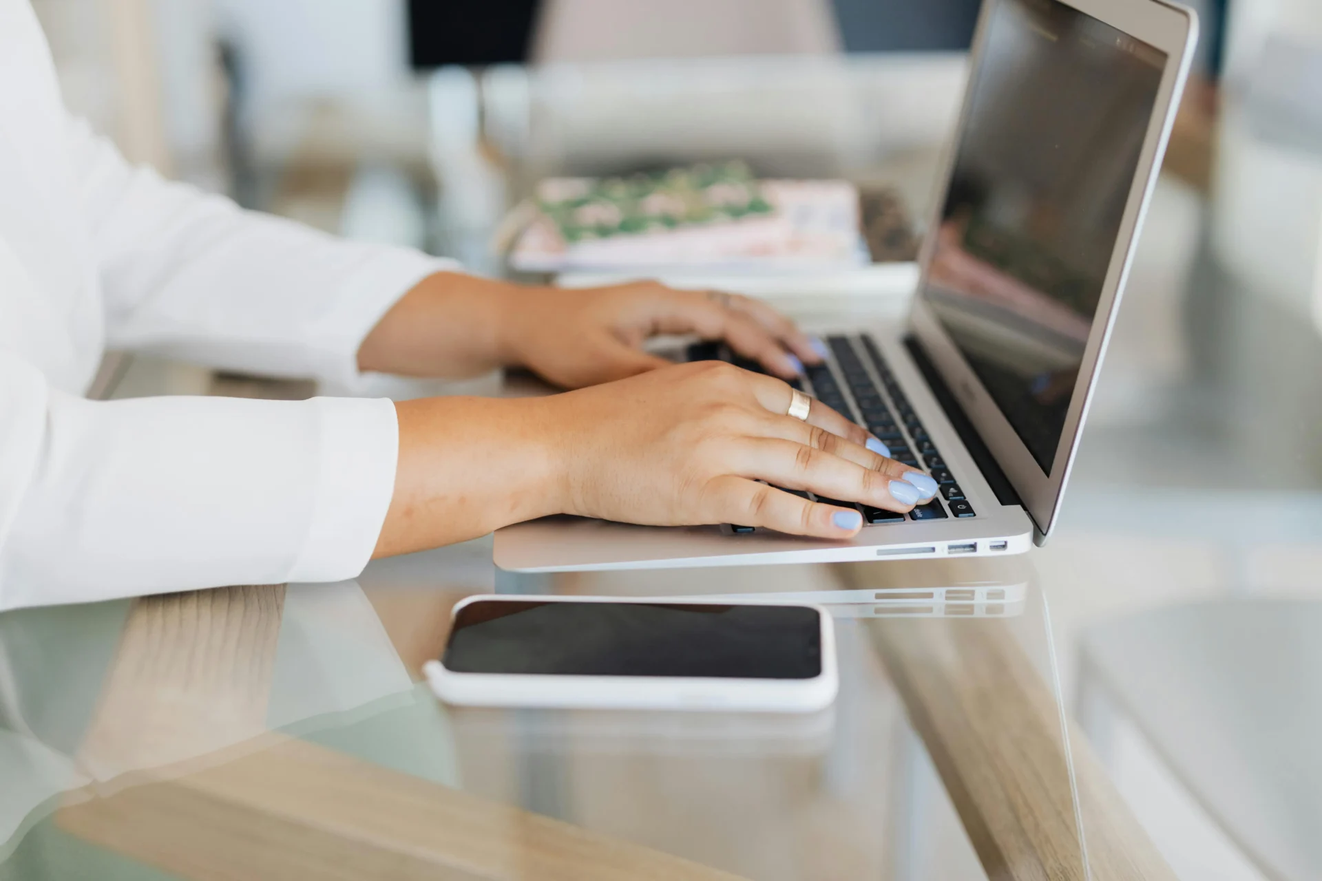Professional woman typing on a laptop beside a smartphone while using an AI brand visibility tracker to manage online brand performance.