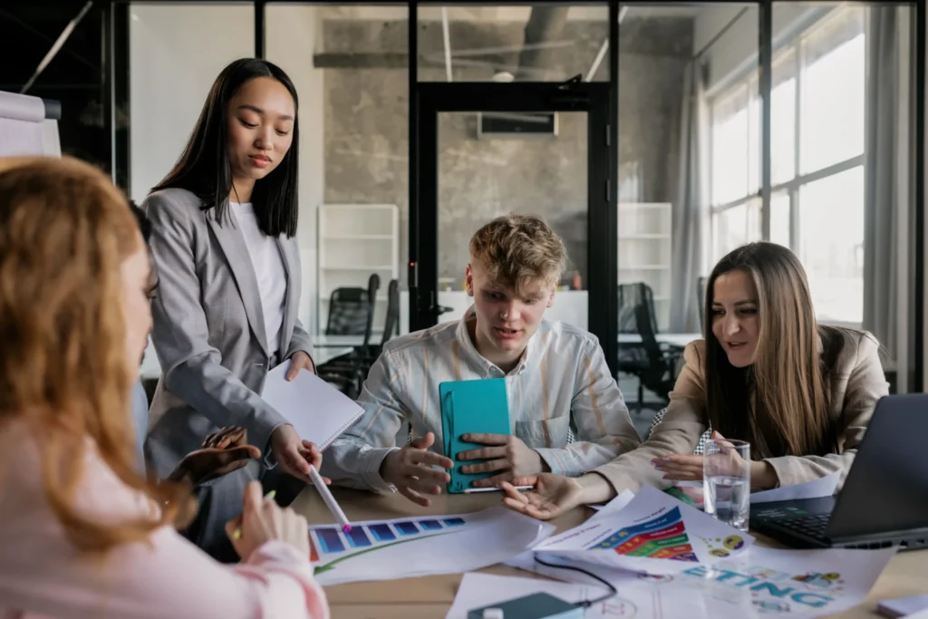 Young marketing professionals analyzing colorful campaign charts and mobile data to evaluate brand vs competitor AI mentions in a modern agency setting.