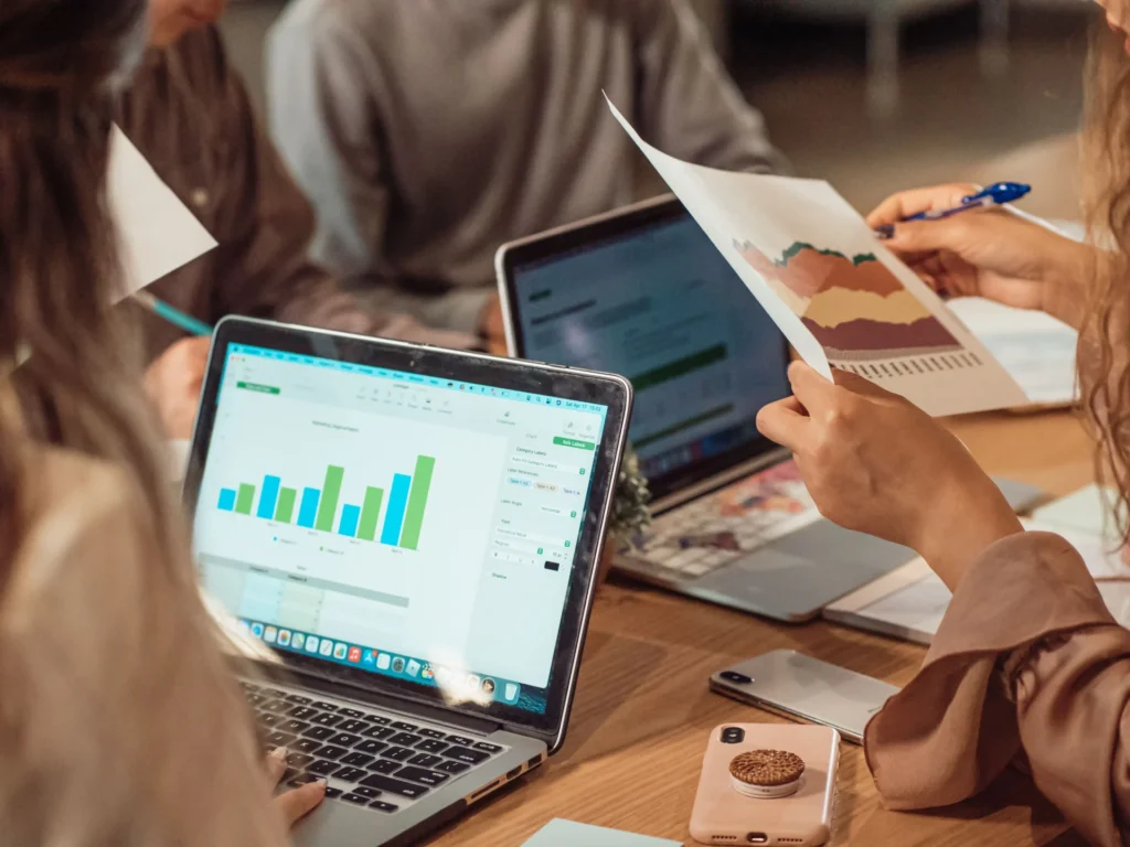 Digital marketing team working with bar chart dashboards on laptops and printed graphs while tracking AI search trends.