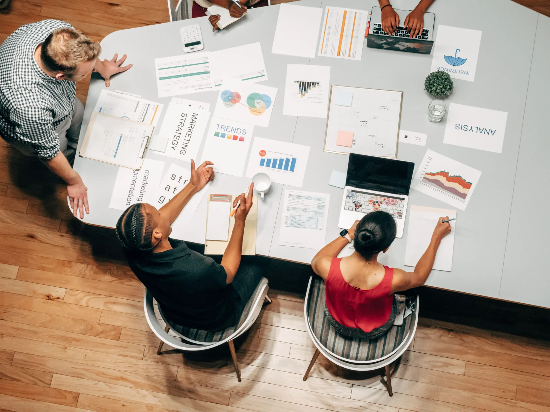 Diverse marketing team collaborating around a table covered with marketing strategy, trends, and analysis documents while working to track AI search impressions.