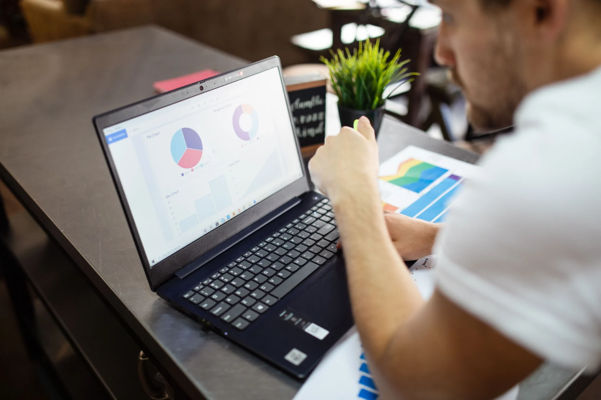 Small business owner reviewing pie chart dashboard on laptop and printed analytics reports to support GEO for small businesses