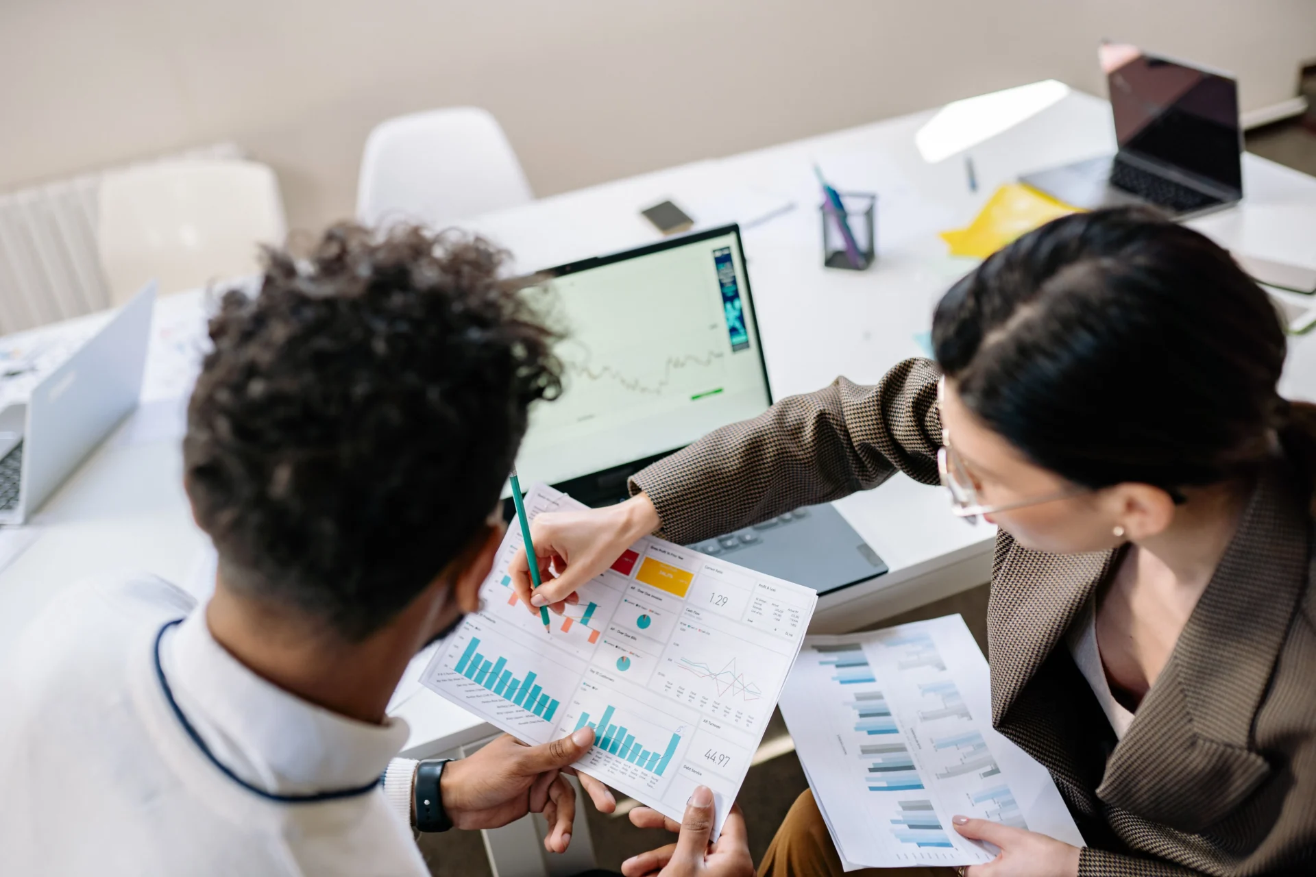 Two marketing professionals reviewing printed data reports and charts while discussing AI search trends in office setting.