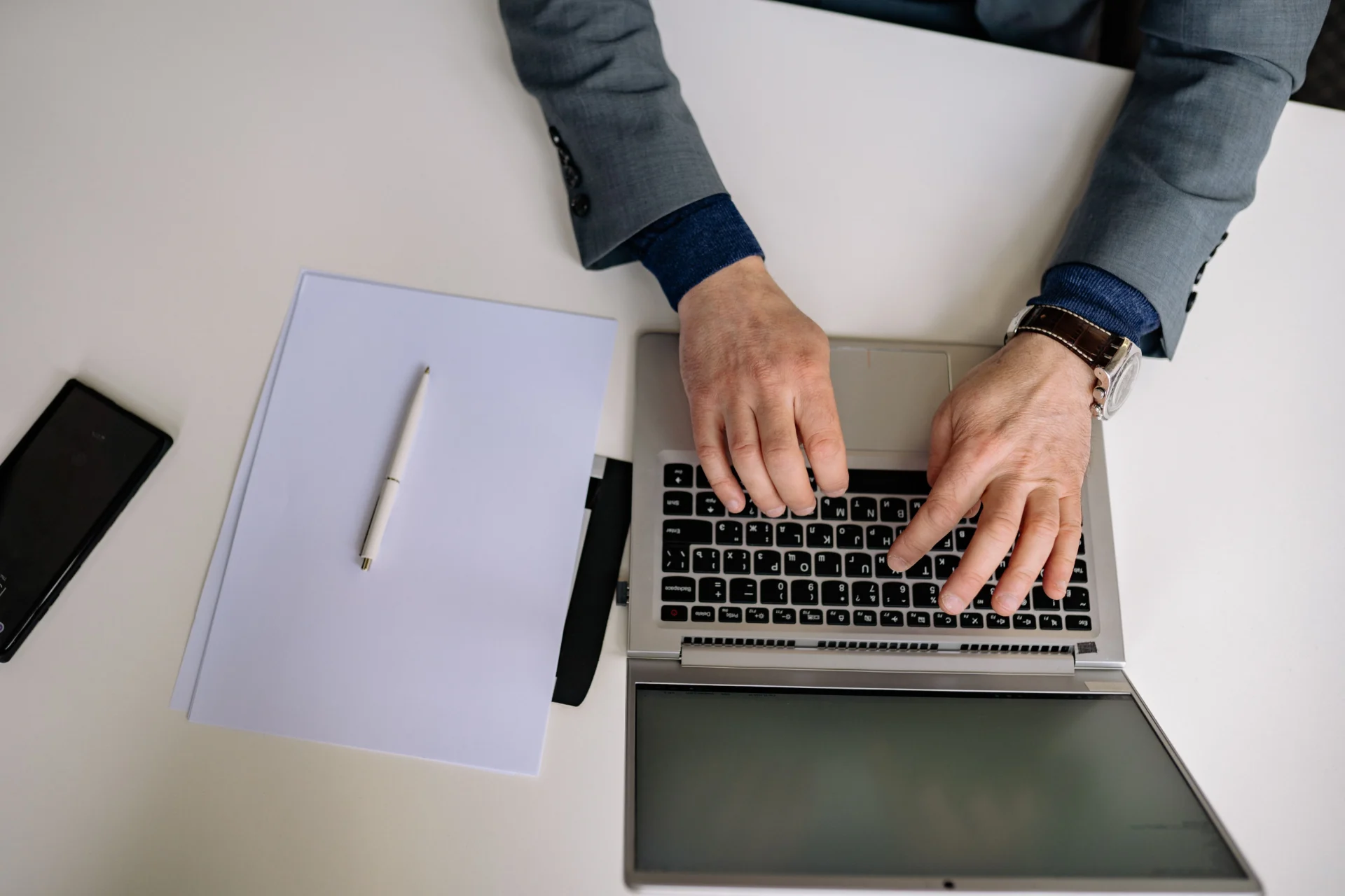 Overhead view of a businessman typing on a laptop beside a notepad, reflecting SEO and GEO fusion copywriting strategies