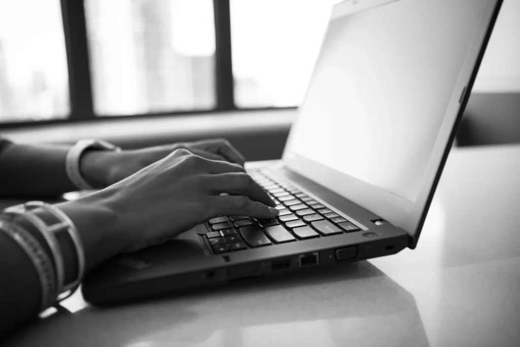 Person typing on a laptop while holding a pen and book, preparing a press release for AI search optimization
