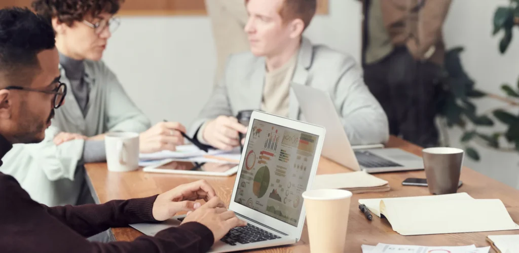 Marketer analyzing detailed dashboards on a laptop while colleagues review reports to measure AI source authority