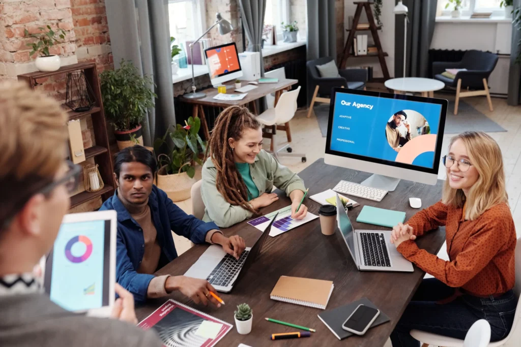 Creative agency team collaborating with laptops and a presentation screen while planning how to optimize testimonials for AI visibility