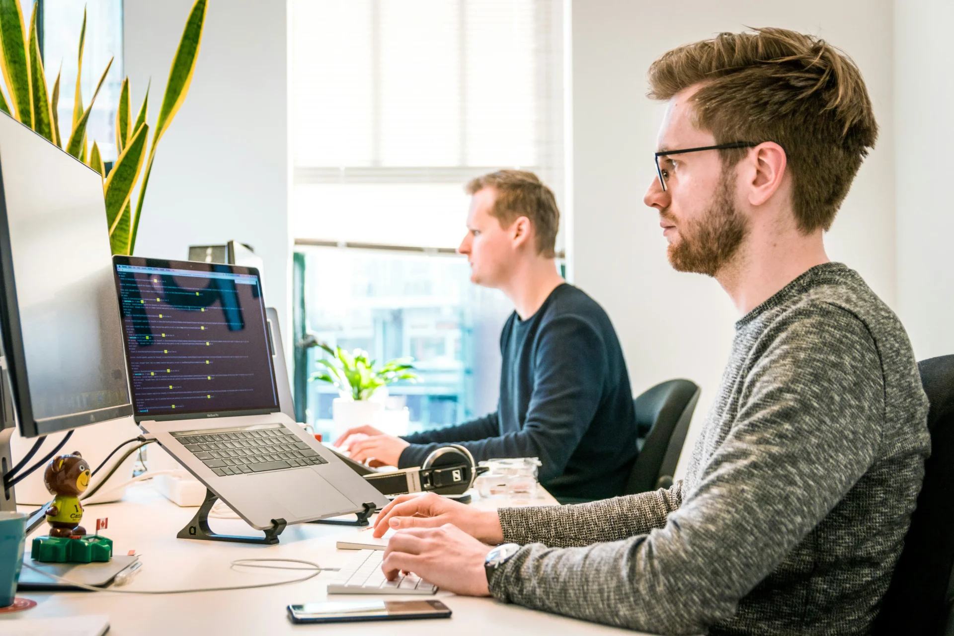 Profile view of a man wearing glasses sitting at a office desk typing on a keyboard in front of multiple display screens, analyzing what makes content citation-worthy for AI systems in GEO.