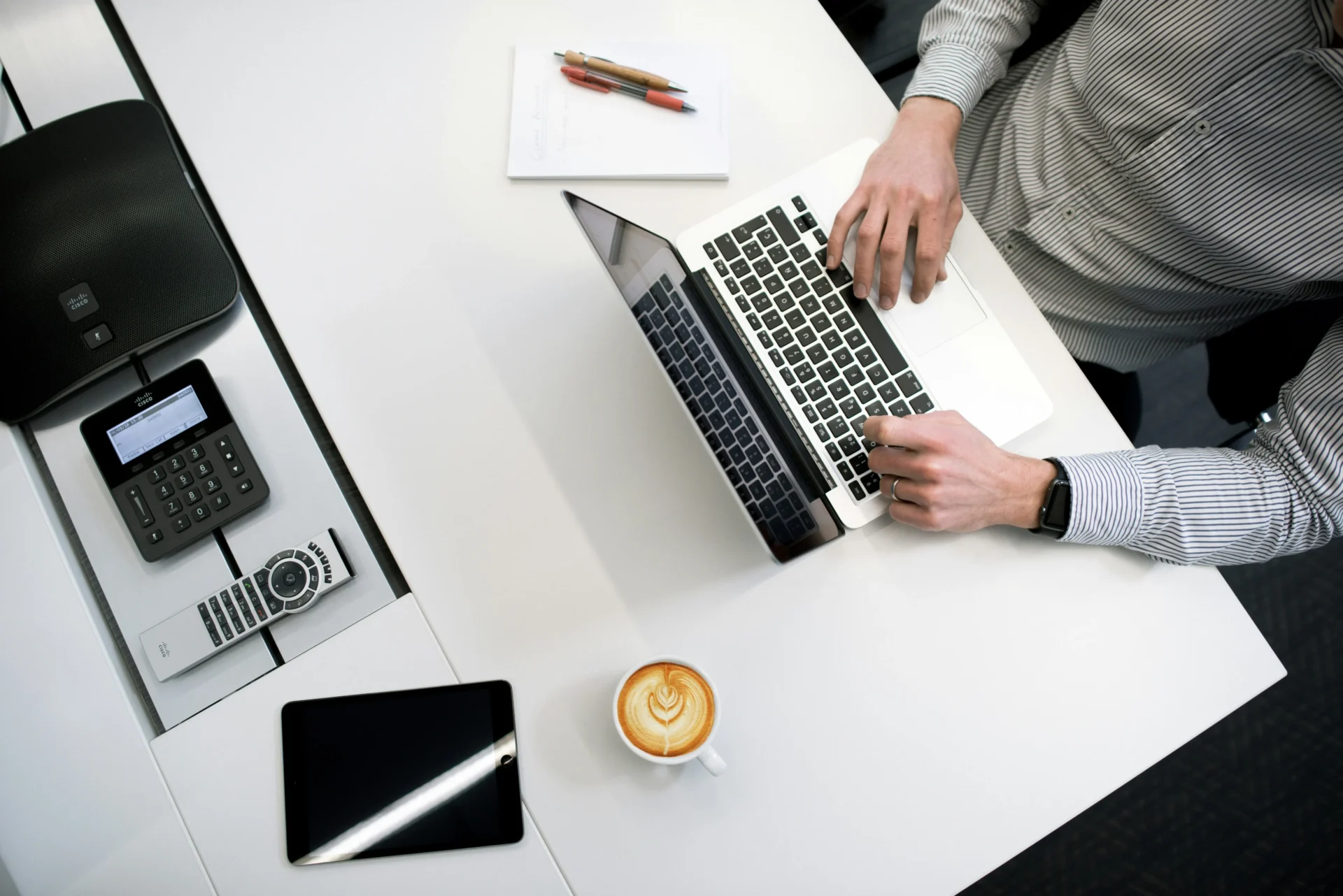 Top-down view of a professional typing on a laptop next to a tablet and coffee while performing a GEO content audit for high-volume search queries.
