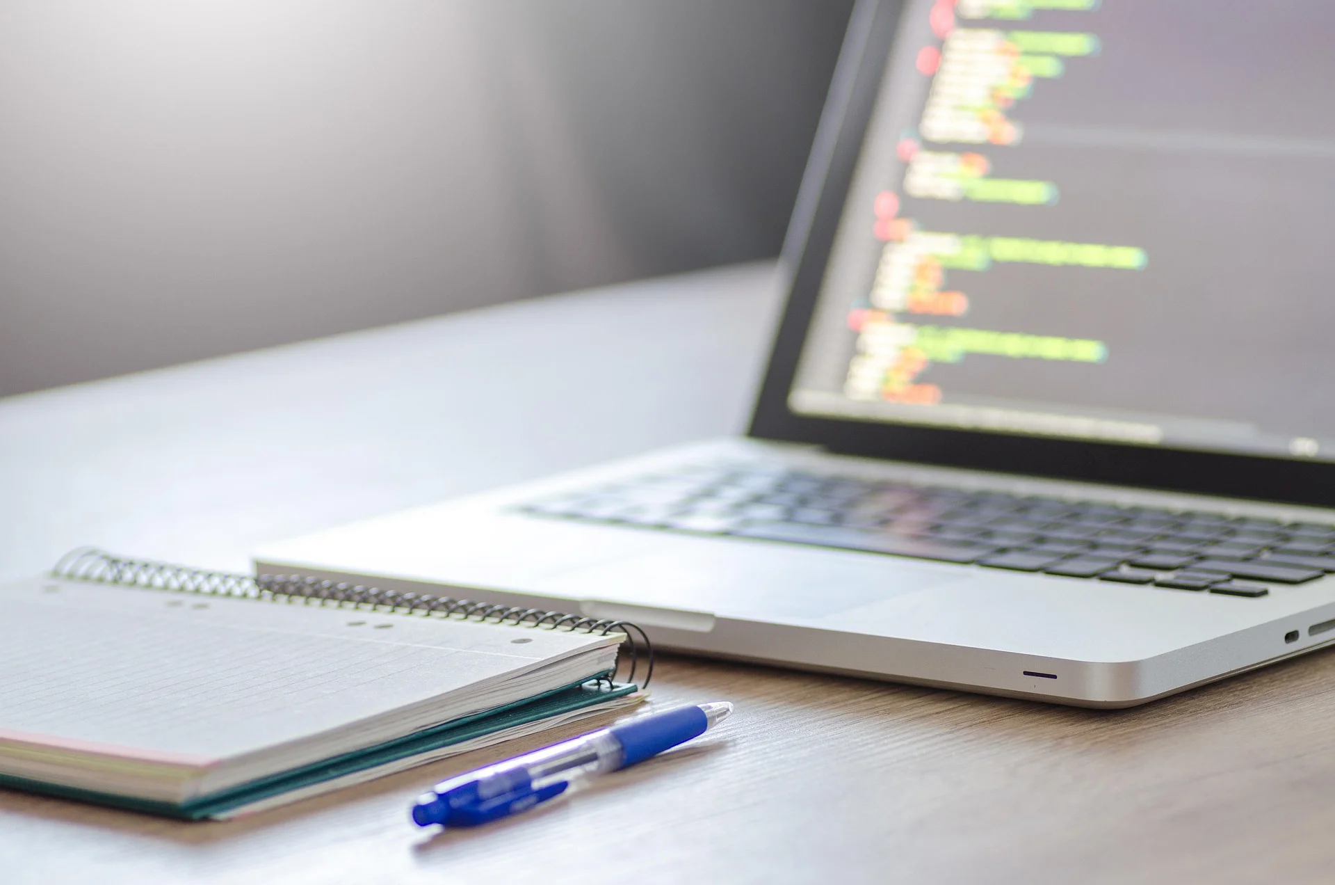 Close-up of laptop screen showing colorful code beside a spiral notebook and pen