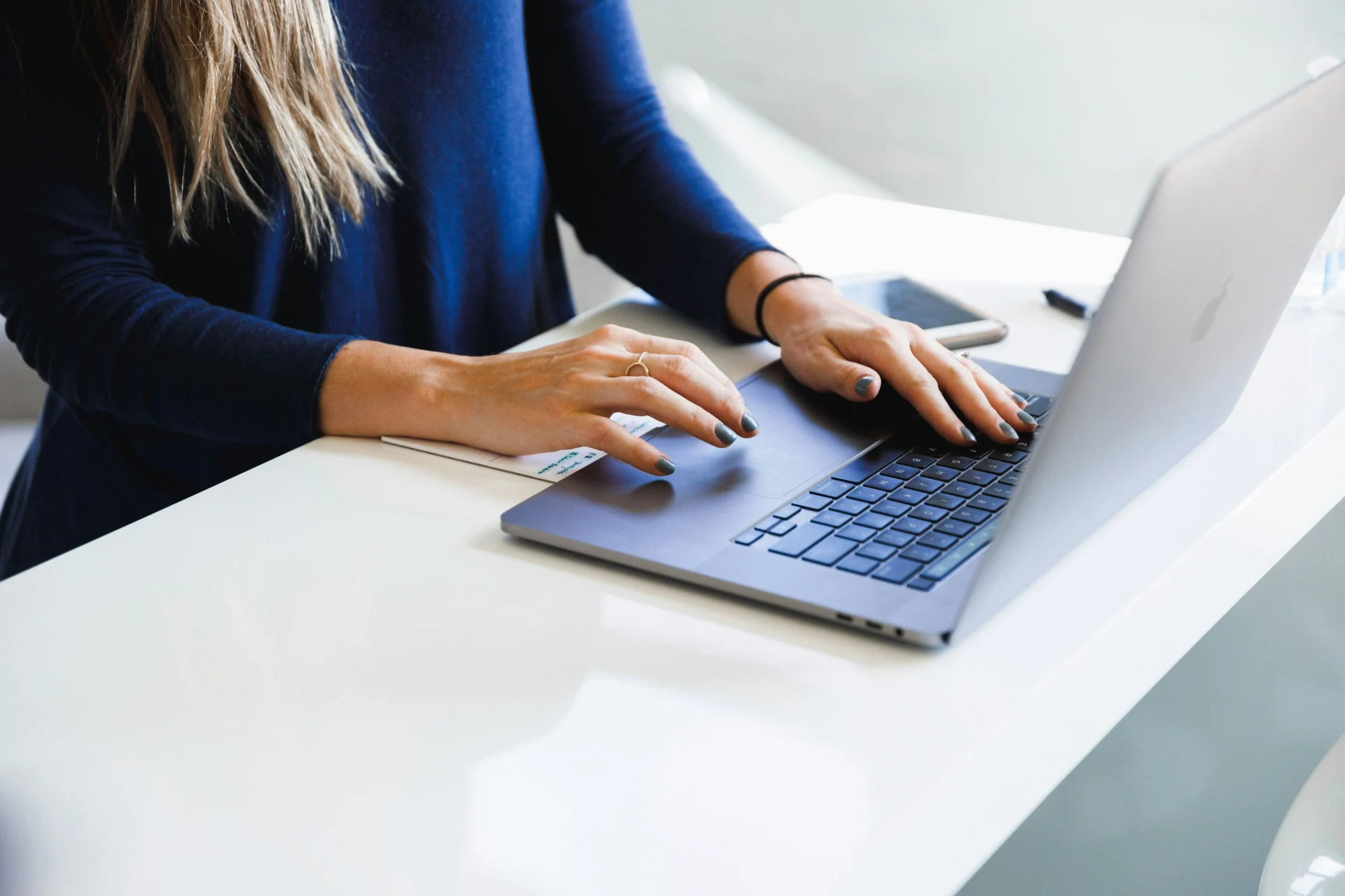 Woman in blue sweater typing on a MacBook trackpad at a white standing desk