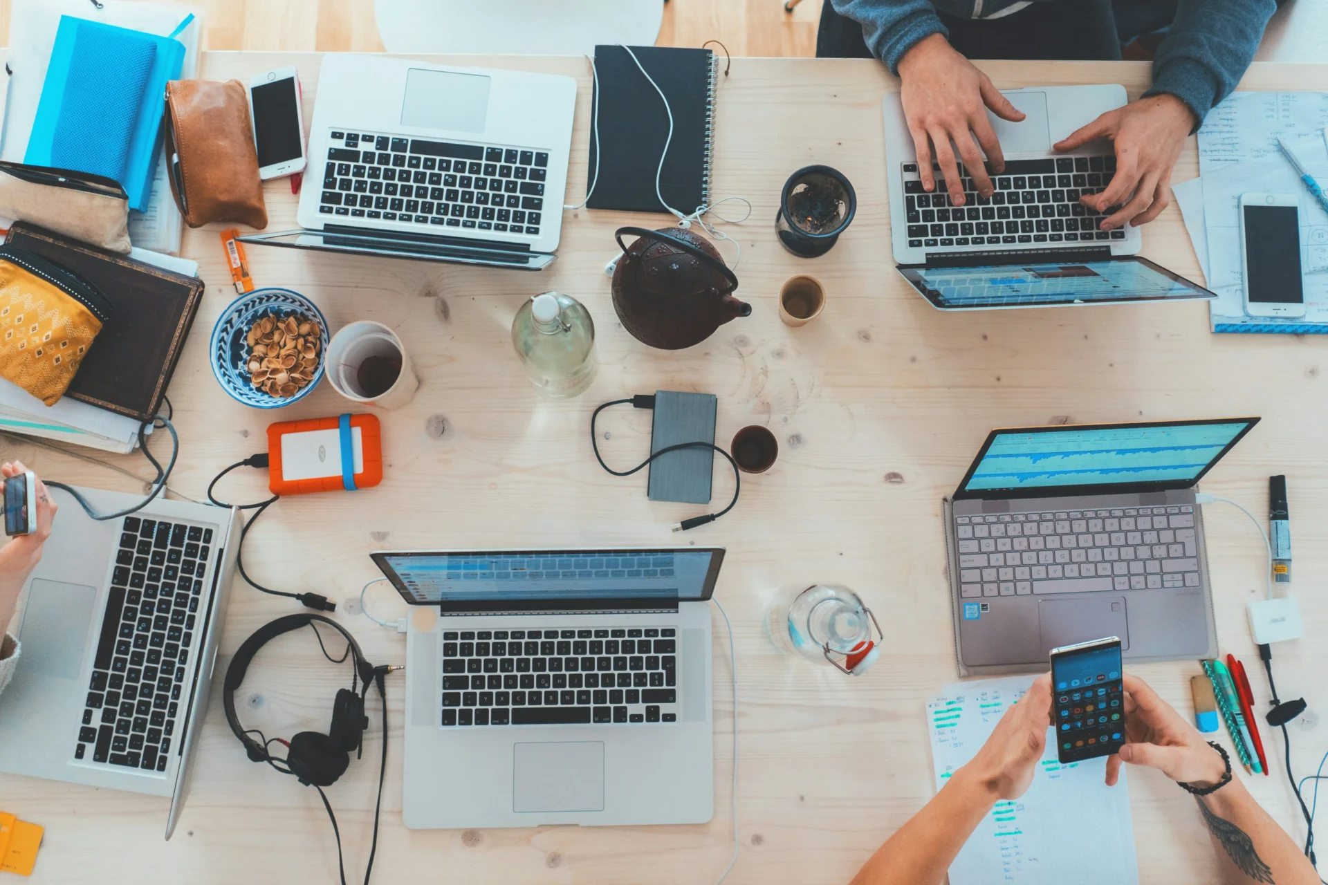 Top-down overhead view of a team working on laptops and smartphones at a large wooden desk, discussing strategy on how to build authority signals for AI citations in GEO.