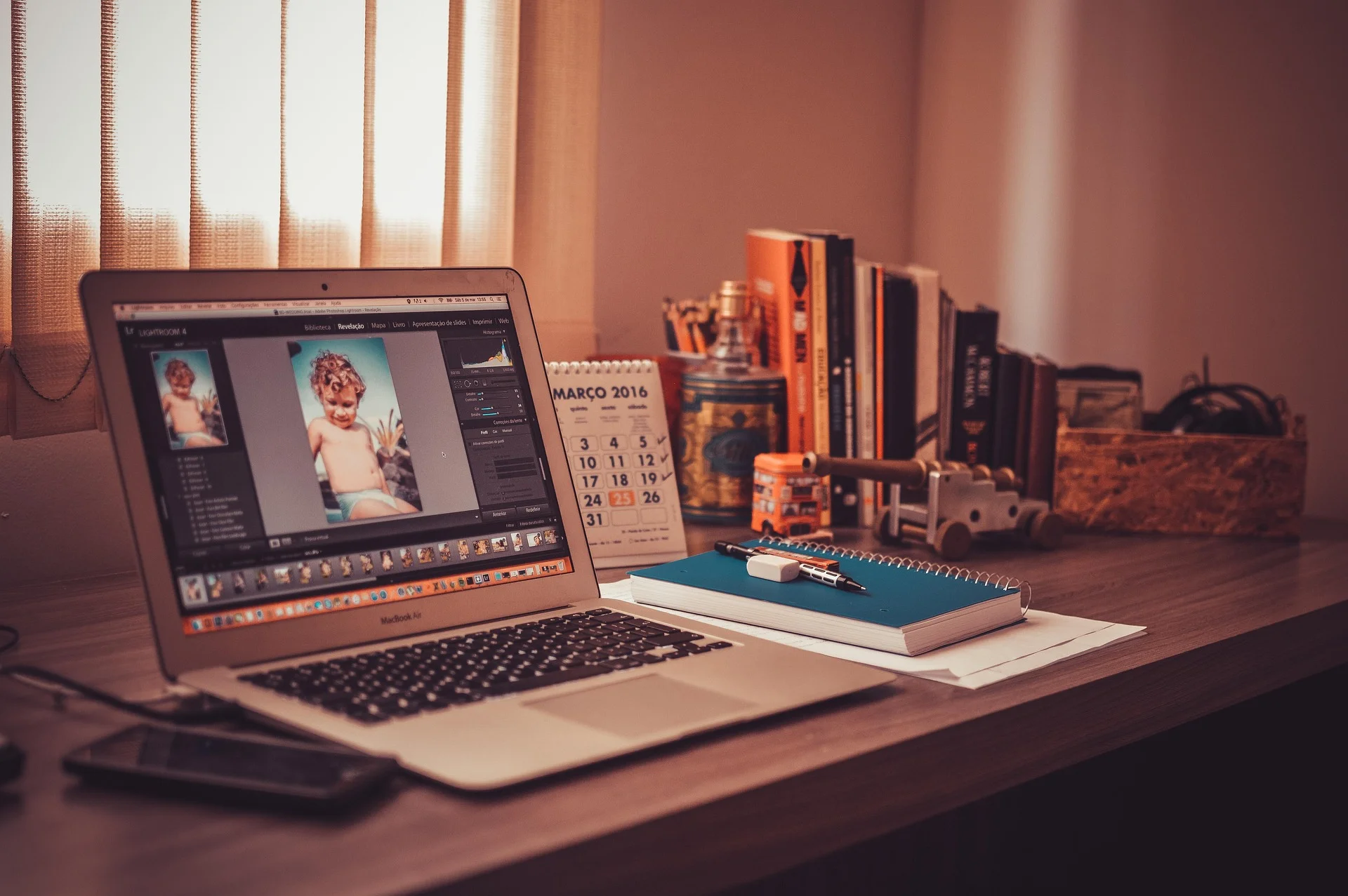 MacBook Air showing Lightroom photo editing next to notebook and calendar on desk