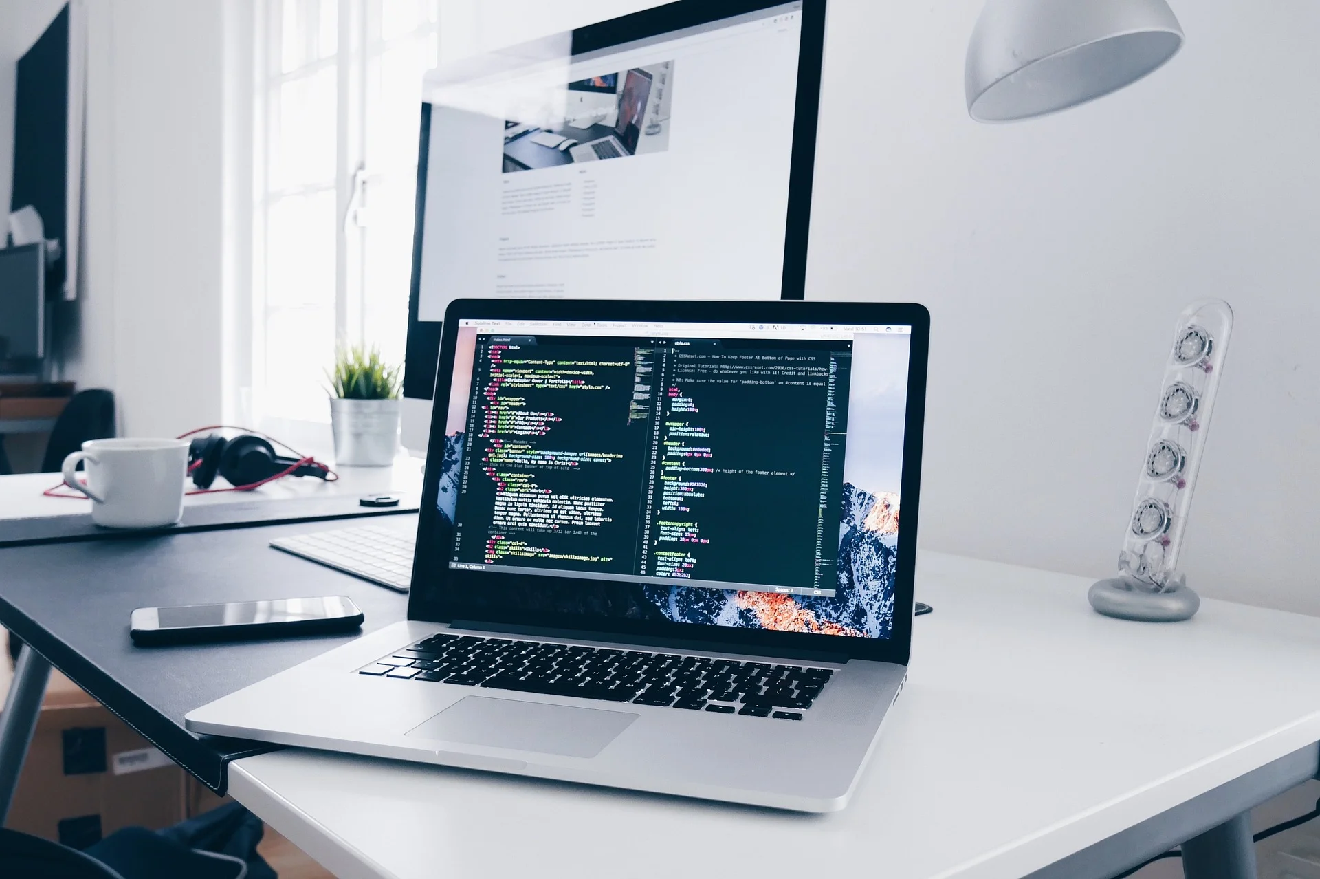 Laptop showing code editor next to a second monitor displaying a website design